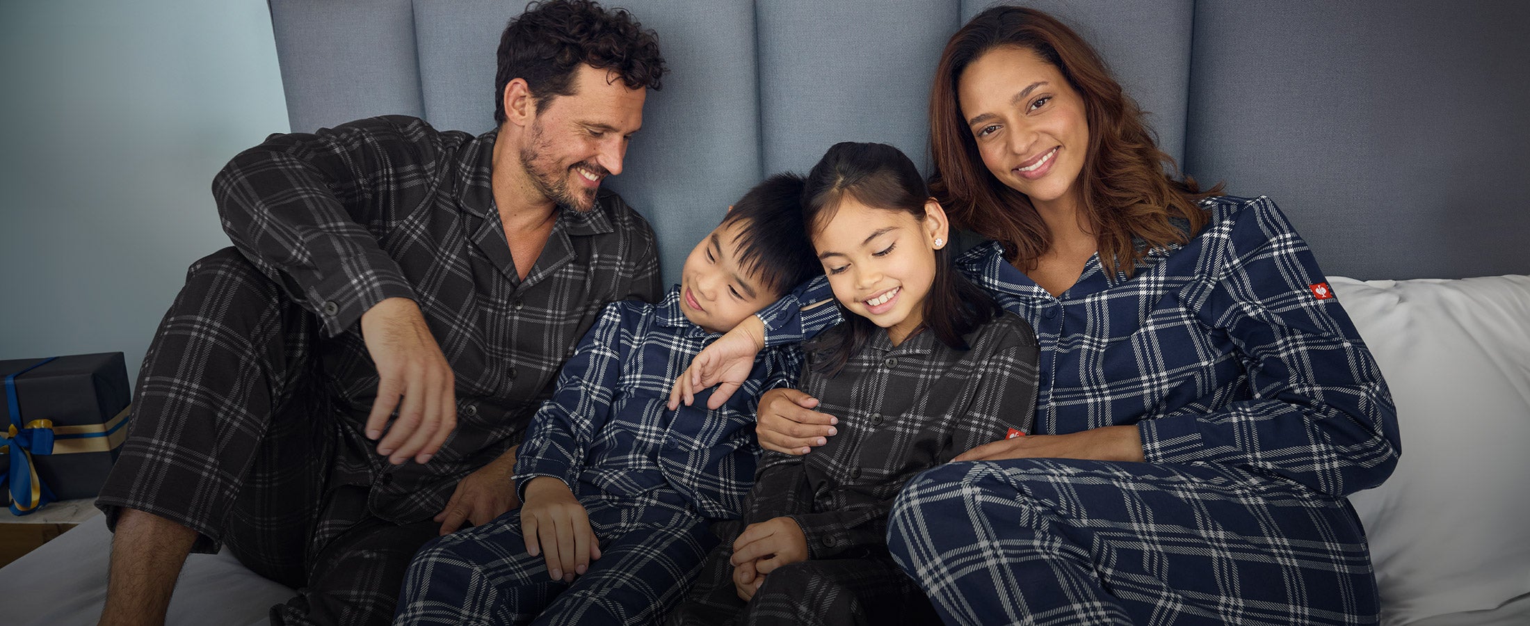 Woman, man, girl, and boy wearing e.s. check pyjamas on a bed