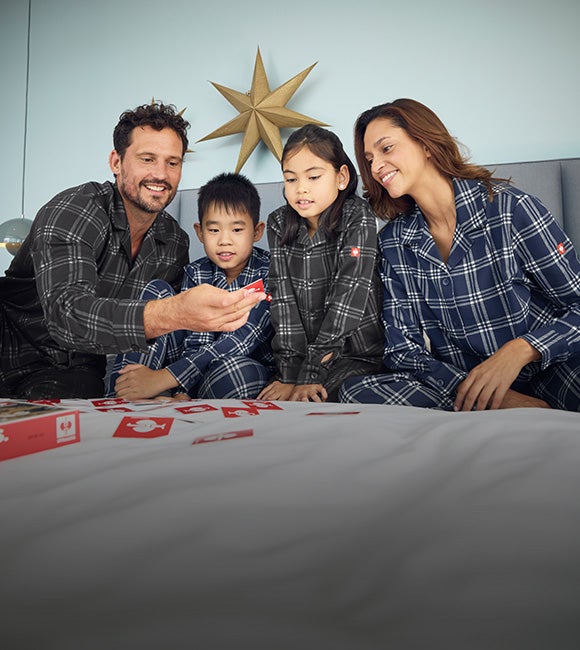 Woman, man, girl, and boy wearing e.s. check pyjamas on a bed