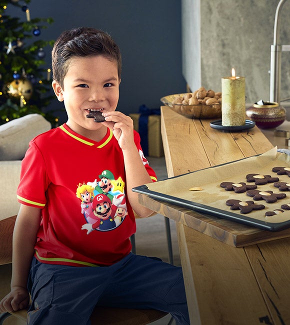 Boy wearing clothing from the Super Mario x Strauss collection sitting at a counter eating cookies
